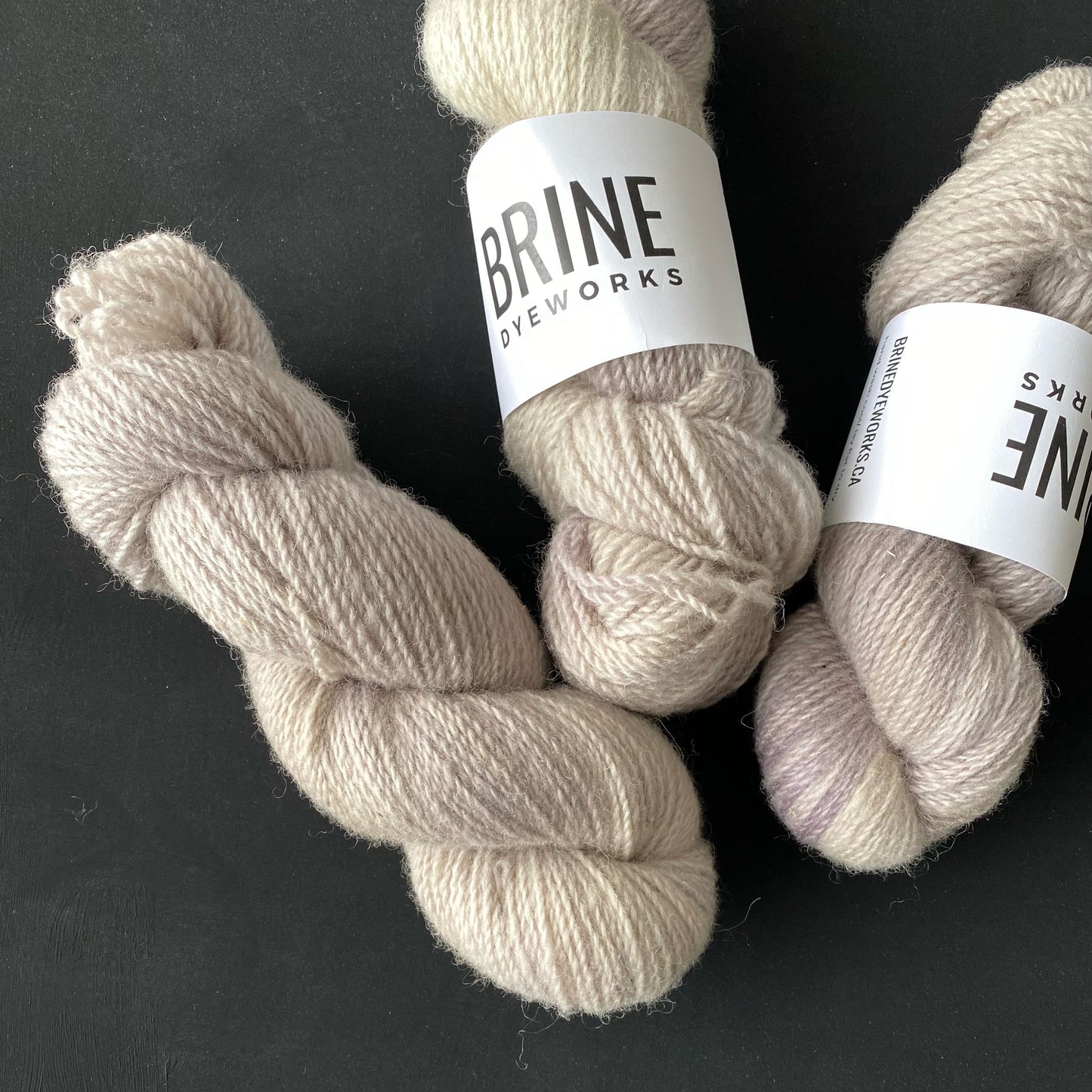 three skeins of light grey yarn on a black background