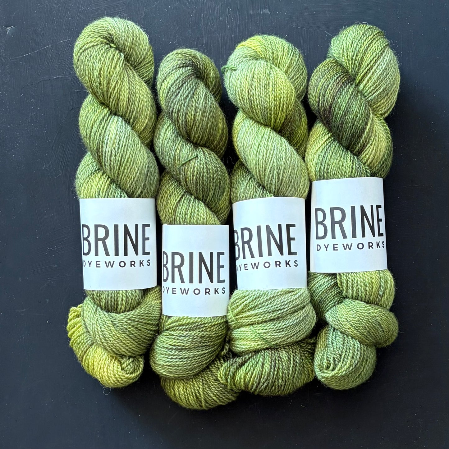 Four skeins of green untreated Blue Faced Leicester wool yarn labeled with the brand name BRINE Dyeworks.