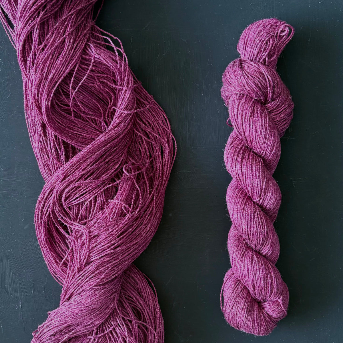 Purple yarn skein and a smaller twisted yarn on a dark surface