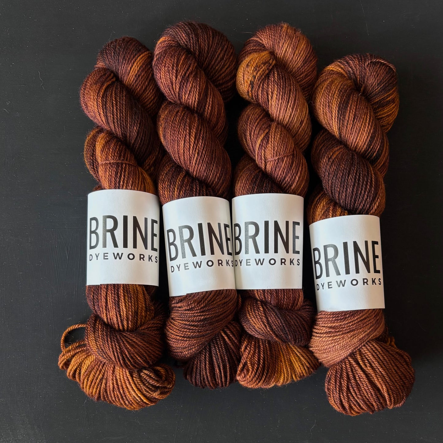 Four skeins of brown yarn with BRINE DYEWORX labels on a dark background
