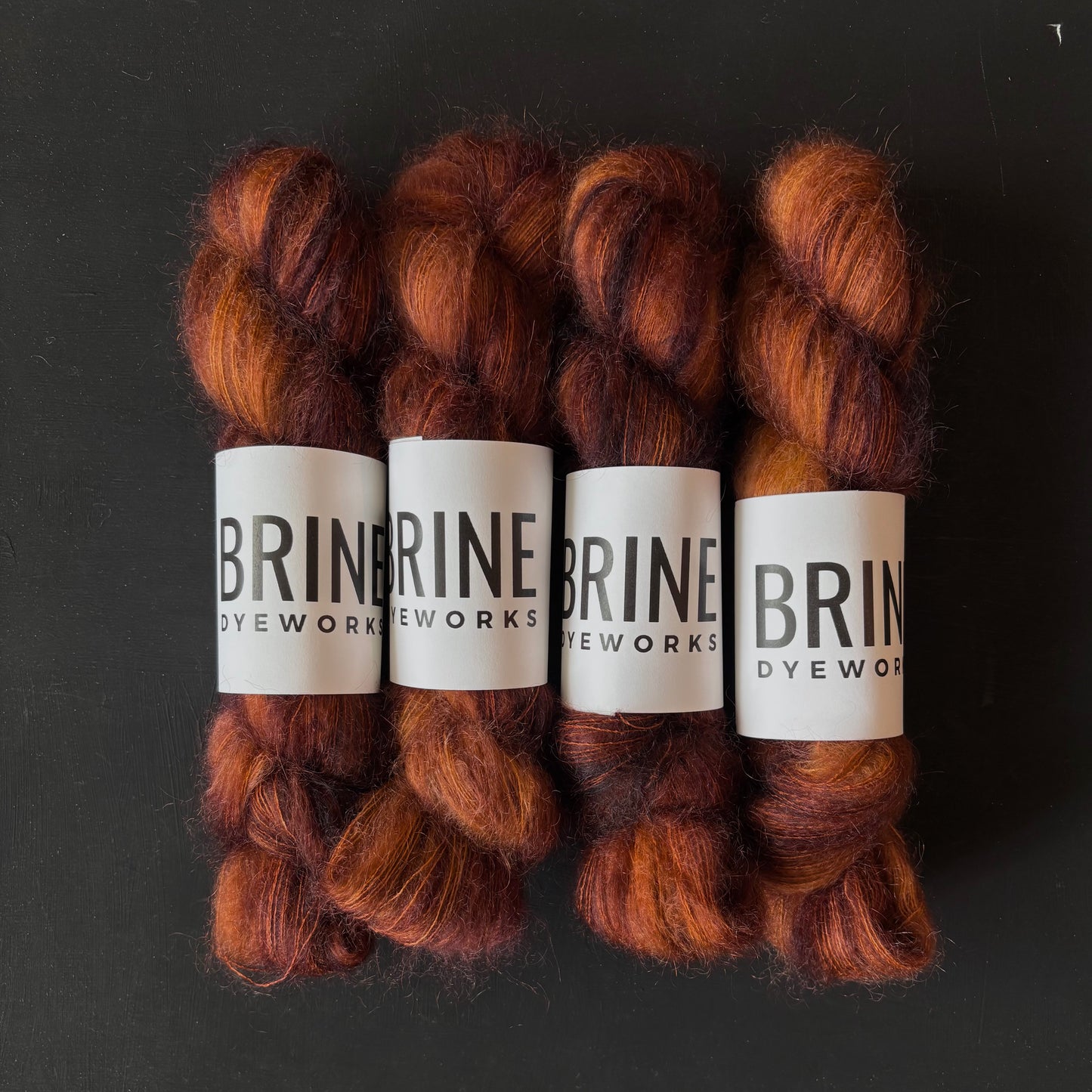 Four skeins of brown mohair yarn with visible labels on a black background