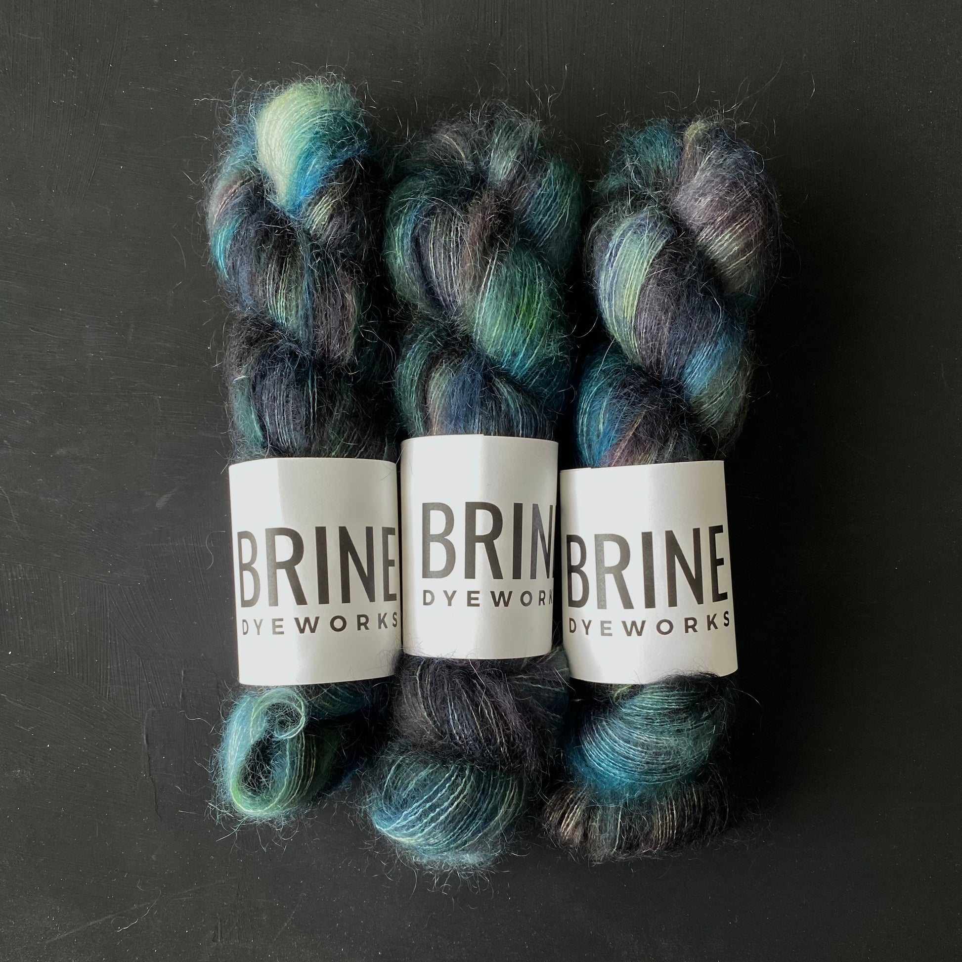 Three skeins of mohair silk lace yarn in shades of blue and green, labeled 'BRINE DYEWORKS'.