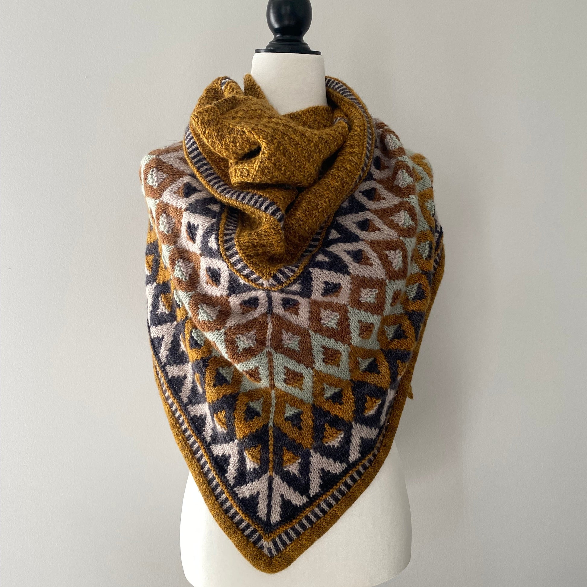 Knitted patterned shawl on a mannequin against a plain background