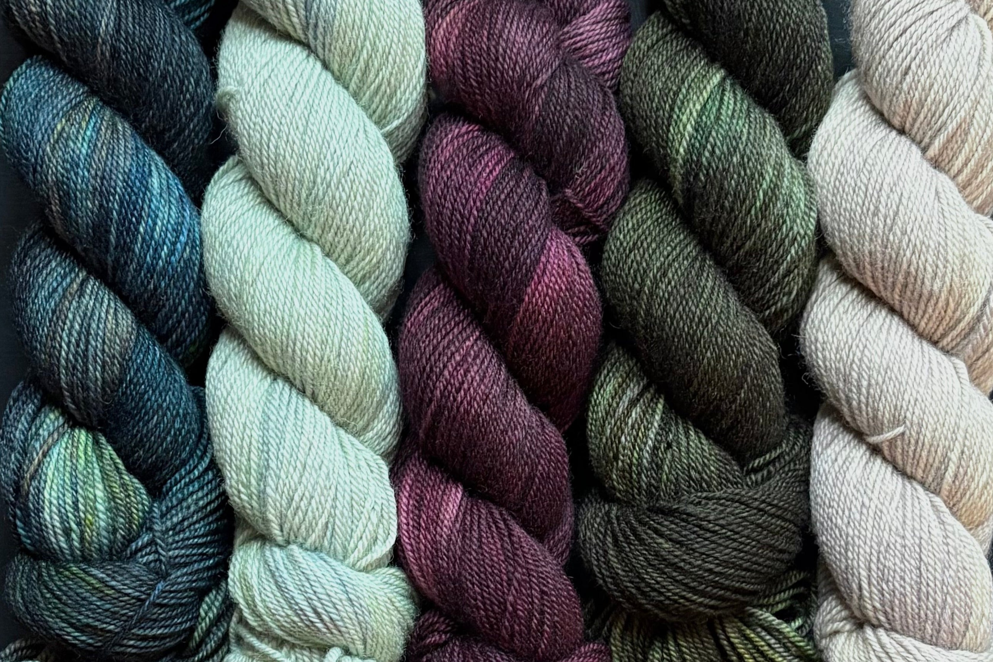 Five skeins of yarn in various colors on a dark background