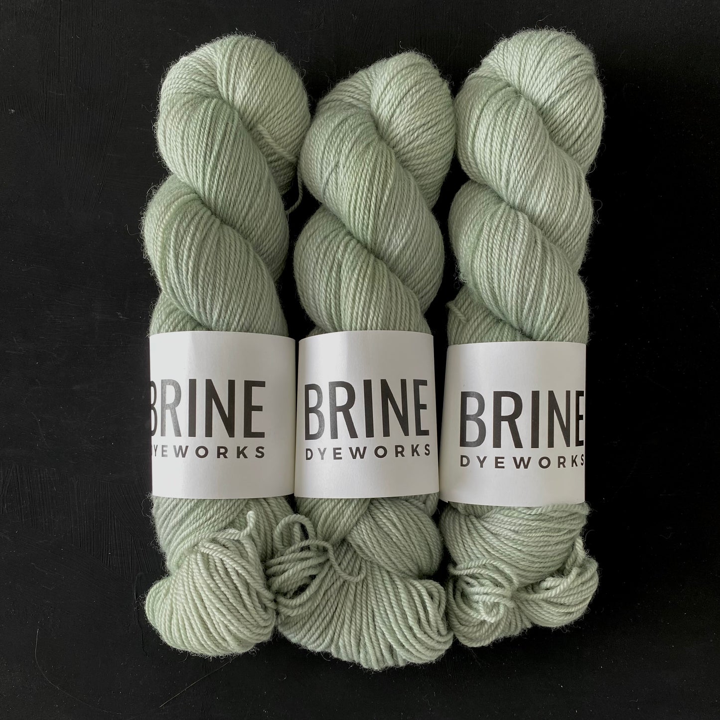 Three skeins of Brine Dyeworks yarn in a matching pale green color, arranged side by side