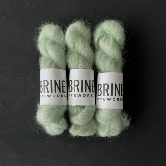 Three Skeins of mohair silk lace yarn in a light green color with Brine Dyeworks labels and a dark background