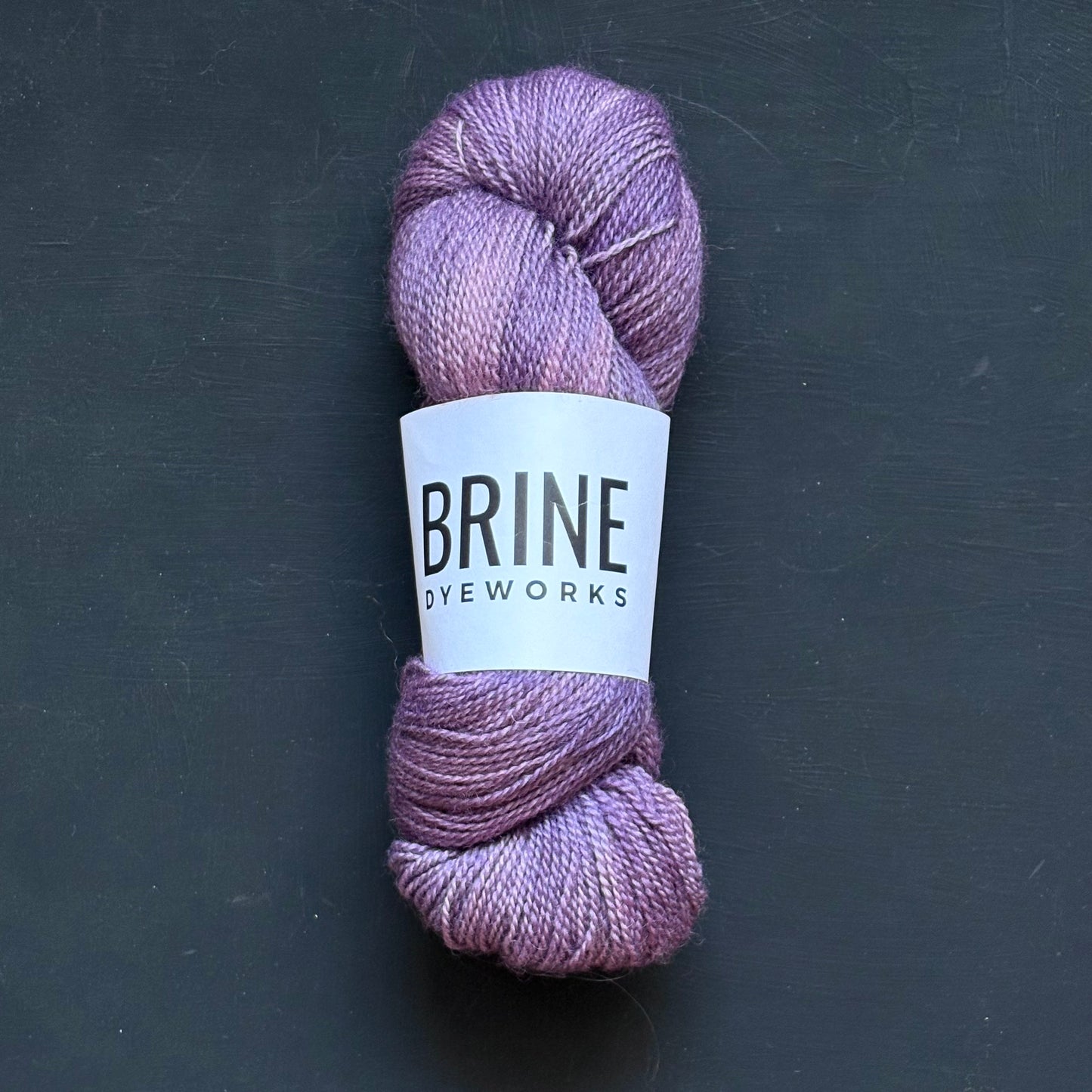 A single skein of purple yarn on a dark background, with a label that reads "Brine Dyeworks"