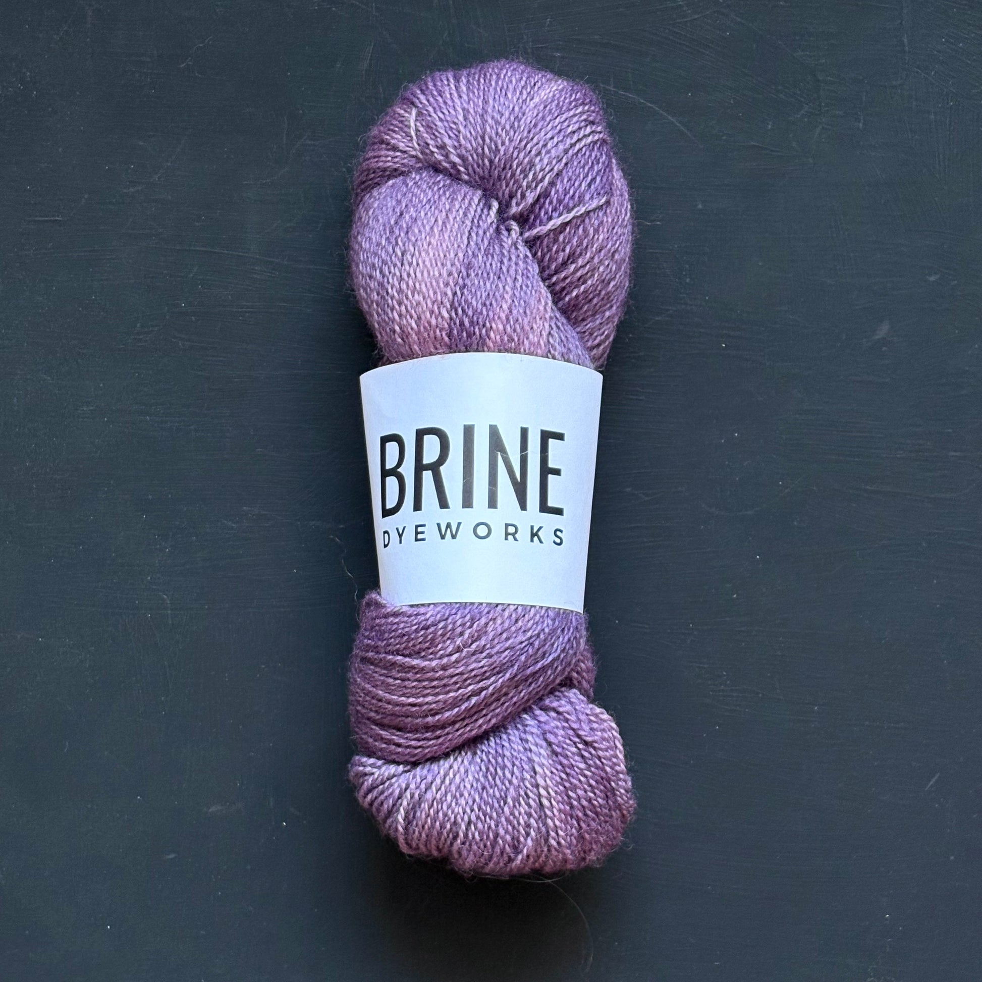 A single skein of purple yarn on a dark background, with a label that reads "Brine Dyeworks"