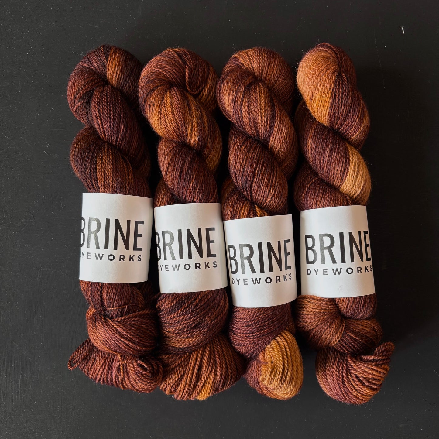 Four skeins of brown yarn with BRINE DYEWORKS labels on a dark background