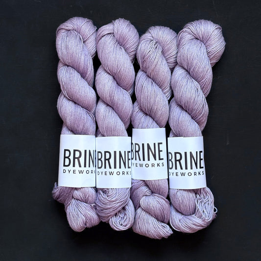 4 skeins of pale purple silk linen sport weight yarn with Brine Dyeworks labels on a dark back ground