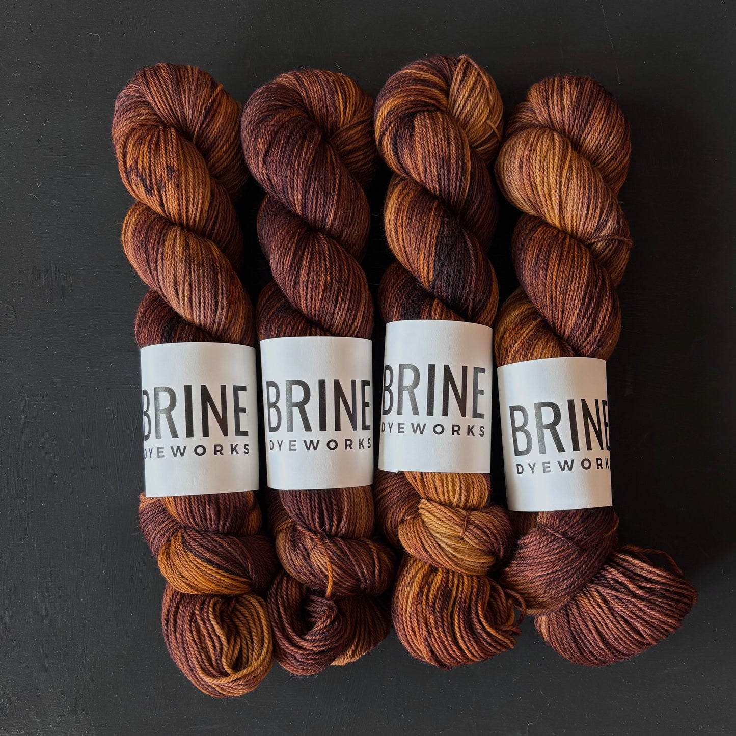 Four skeins of brown yarn with visible labels on a dark background