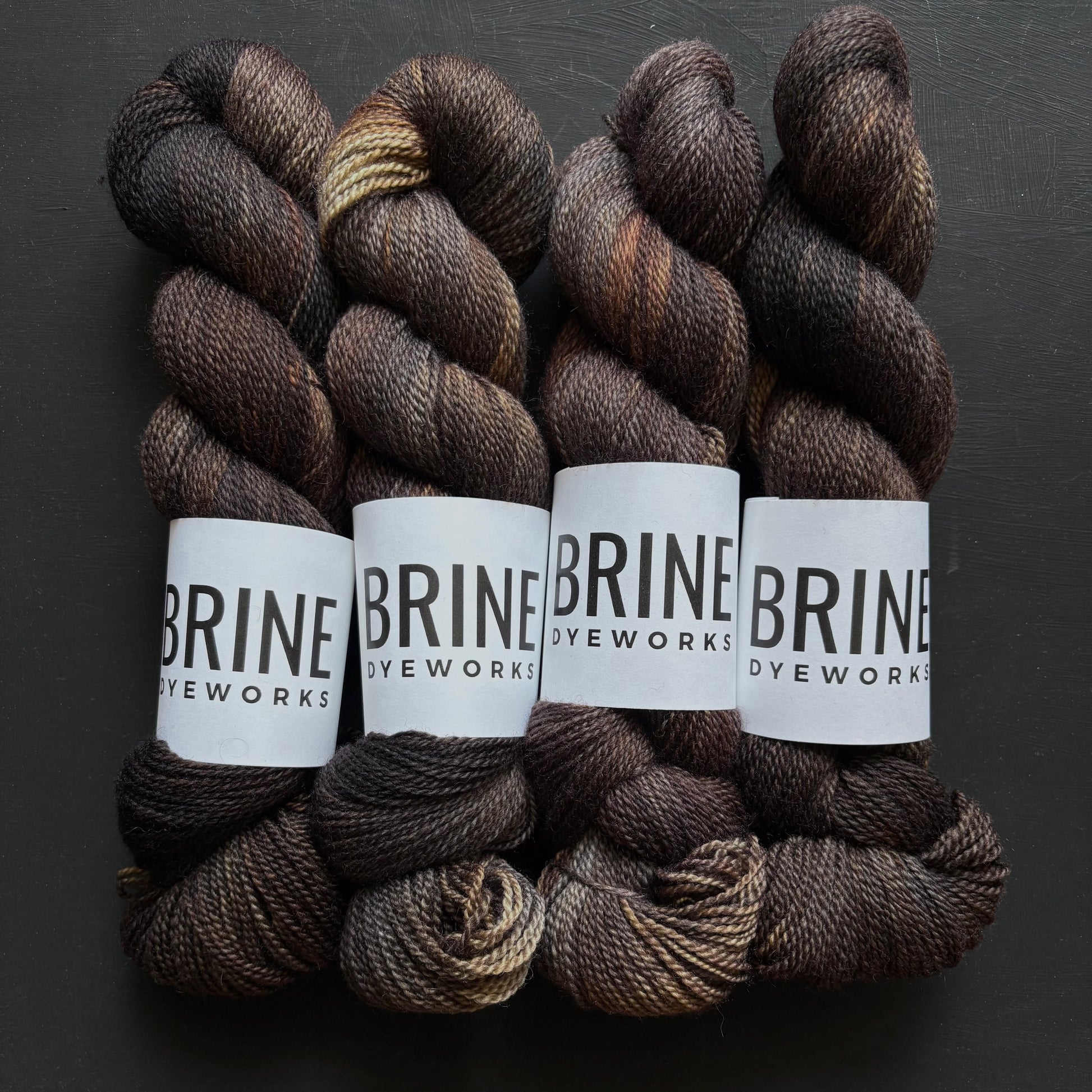 Four skeins of dark brown yarn with BRINE DYEWORX labels on a dark background