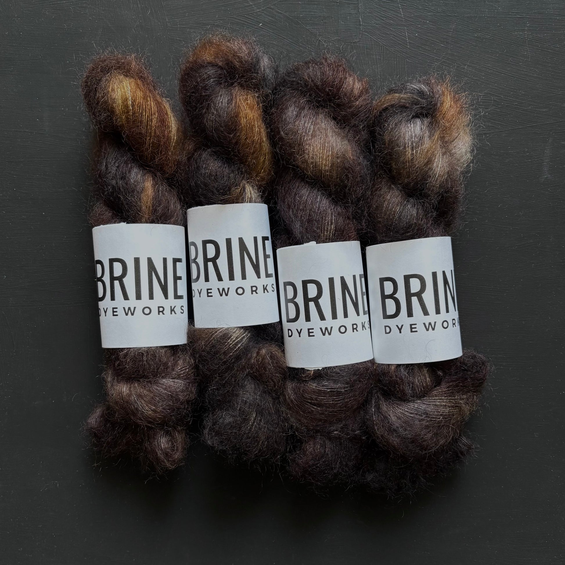 Four skeins of dark brown mohair yarn with 'Brine Dyeworks' labels on a dark background