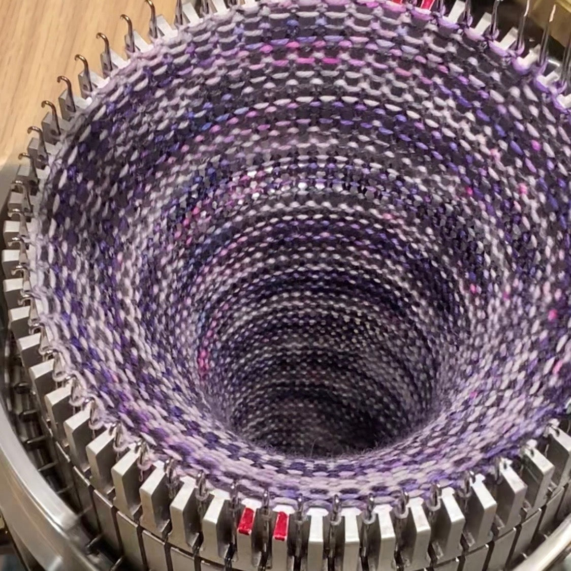 yarn being knit into a sock tube on a circular knitting machine